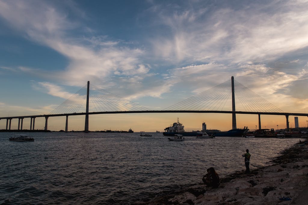 Beautiful view of a suspension bridge in Cebu City during dusk with boats and calm sea.